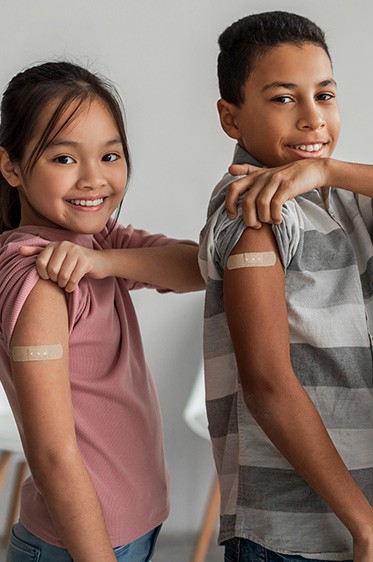 a boy and girl smiling with a bandaid on their arm