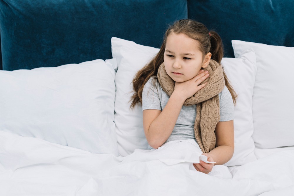 young girl sitting in bed with her hand around her neck